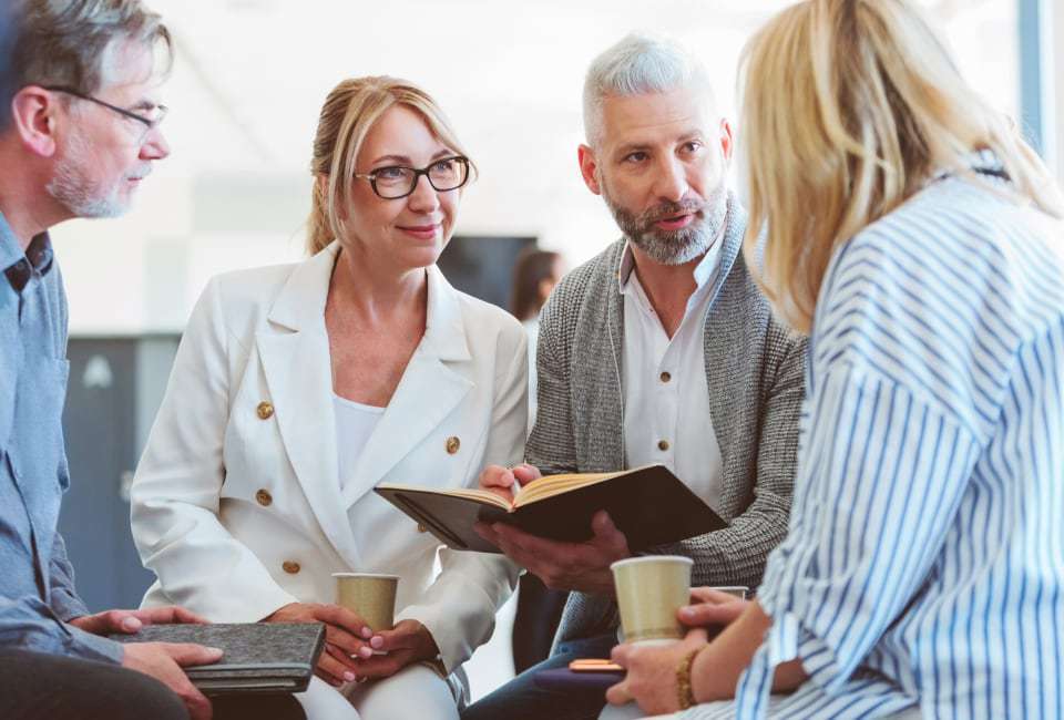 Vier Personen sitzen zu einer Besprechung gemeinsam am Tisch